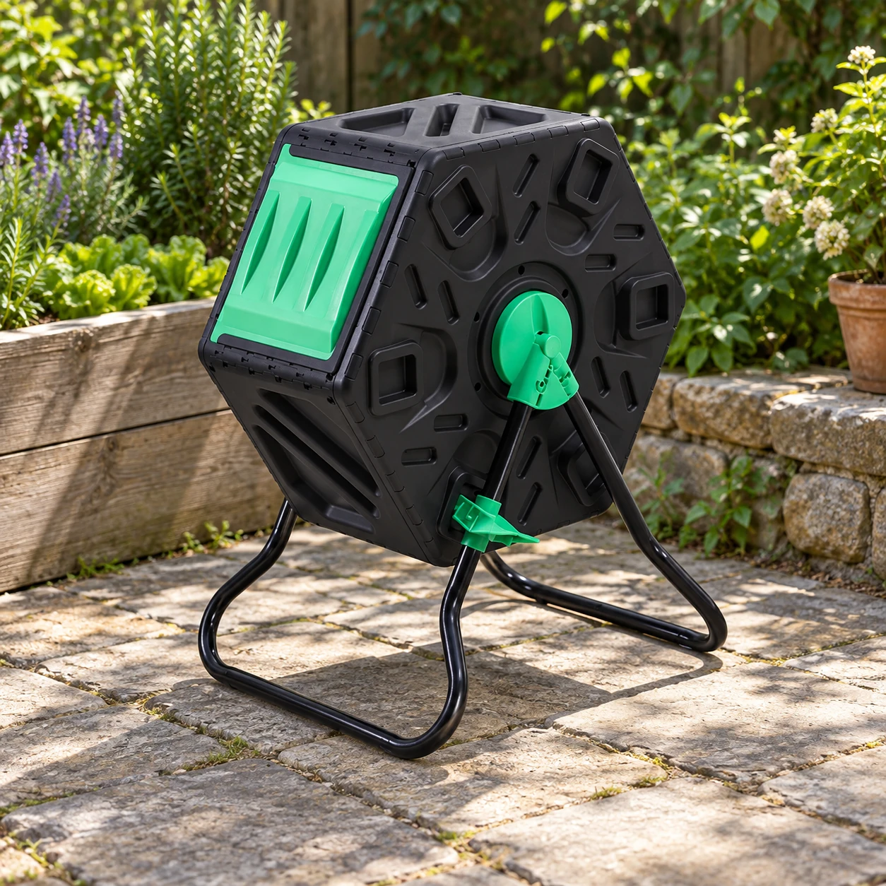 Black and green 65 L compost tumbler standing on a stone path in an established garden