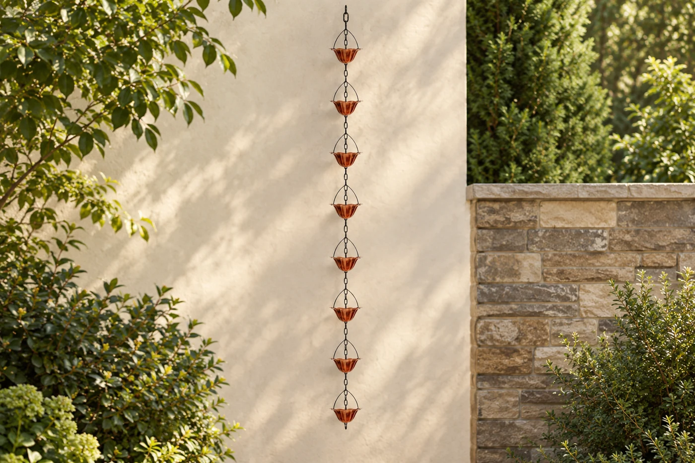 Eight copper-tone rain-chain cups hanging in a leafy garden setting