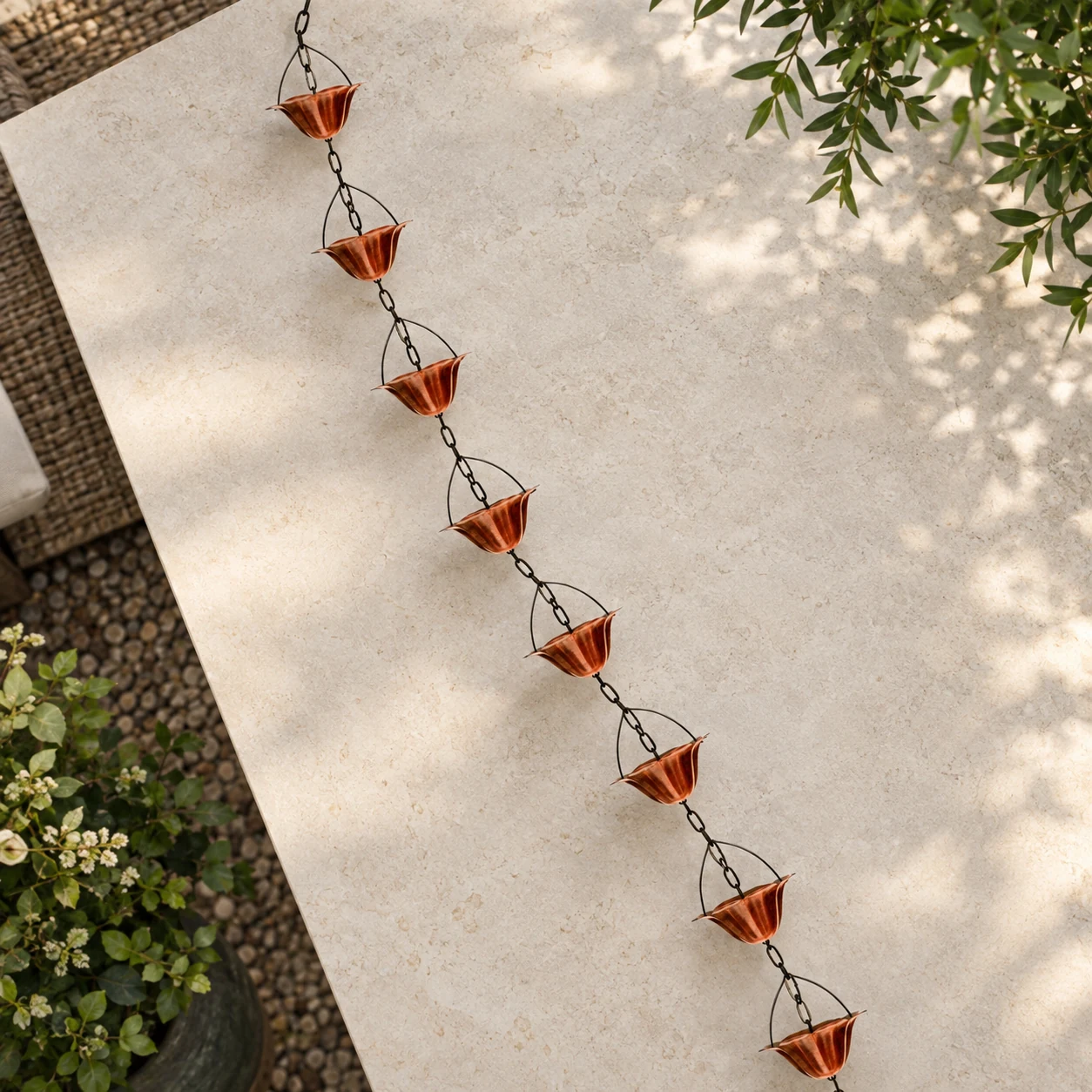 Eight-cup copper-tone rain chain arranged across pale stone